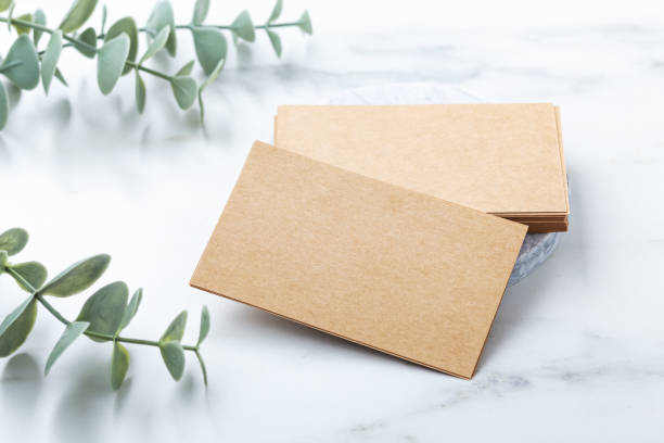 A stack of brown kraft business cards beside eucalyptus leaves